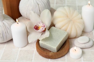 Spa taşlı bitkisel poşetler, sabun, banyo süngeri ve bej kaplamalı yanan mumlar.