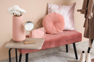 Bej duvarın yanında rahat bir bank, ayakkabılar ve halı.