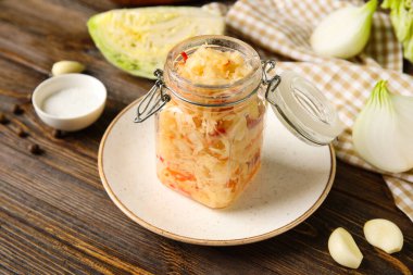 Kavanozda lezzetli lahana turşusu tabakta ve ahşap arka planda malzemeler