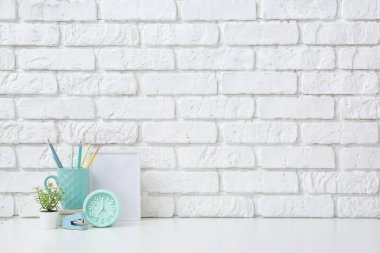 Çalar saati, kırtasiyesi ve ofisteki beyaz tuğla duvarın yanındaki tesisi olan modern bir işyeri.