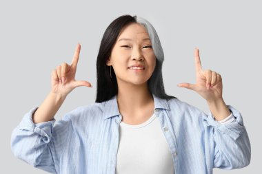 Genç ve yaşlı Asyalı bir kadının gri arka plandaki bir şeyi gösteren portresi.