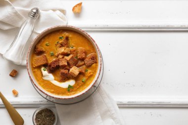 Beyaz ahşap zemin üzerinde kızarmış ekmeklerle bir kase lezzetli krema çorbası.