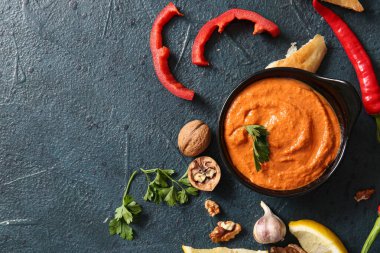 Bir kase lezzetli muhammara ve siyah arka planda malzemeler.