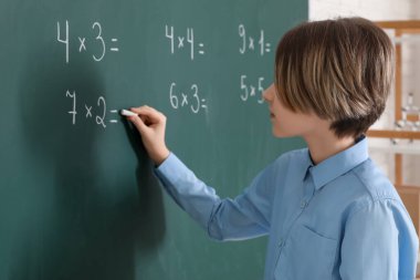 Sınıfta ders sırasında tahtaya yazı yazan sevimli çocuk.