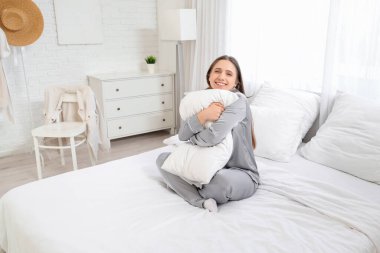 Yatak odasında yastığa sarılan genç bir kadın.