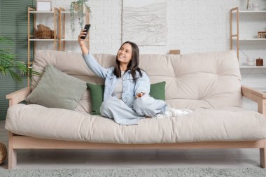 Oturma odasındaki koltukta cep telefonuyla selfie çeken genç bir kadın.
