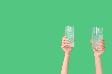 Yeşil arka planda su bardakları olan kadın eller, yakın plan.