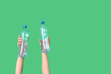 Yeşil arka planda su şişeleri olan kadın eller, yakın plan.