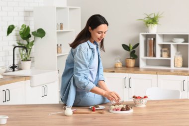 Güzel genç bayan mutfakta çikolata kaplı çilek hazırlıyor.