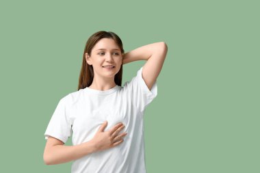 Genç kadın yeşil arka planda göğüslerini kontrol ediyor.