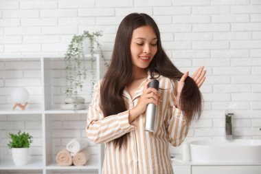 Güzel, genç, mutlu bir kadın evde saç spreyi sıkıyor.