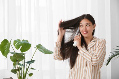 Güzel, genç, mutlu bir kadın evde saç spreyi sıkıyor.