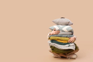 Farklı battaniye ve yastıklarla bej arka planda oturan güzel genç bir kadın.