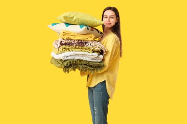 Sarı arka planda farklı battaniye ve yastıklarla dolu güzel, genç ve mutlu bir kadın.