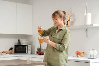 Genç bir kadın mutfaktaki çaya bal ekliyor.