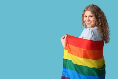 Mavi arka planda LGBT bayrağı olan mutlu genç bir kadın.