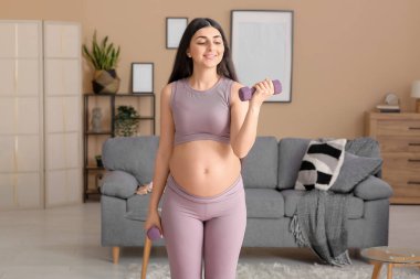 Güzel hamile kadın evde dambıllarla egzersiz yapıyor.