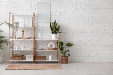 Odadaki beyaz tuğla duvarın yanında heykelciği ve bitkisi olan raf ünitesi.