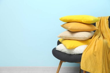 Mavi duvarın yanındaki koltukta yastık ve ekose yığını.