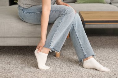 Evdeki kanepede yaya olarak acı çeken genç bir kadın, yakın plan.