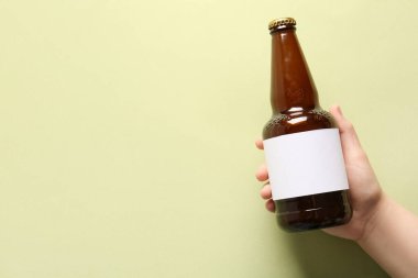 Yeşil arka planda soğuk bira şişesi olan bir kadın eli.