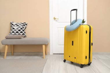 Koridorun girişinde sarı valiz ve boyun yastığı. Seyahat kavramı