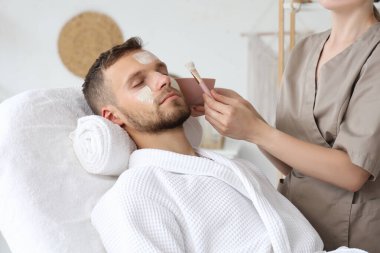 Güzellik uzmanı spa salonundaki adamın yüzüne maske takıyor.