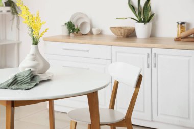 Hafif mutfaktaki yemek masasında mimoza çiçekleri olan vazo.