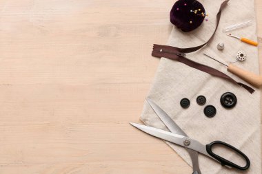 Tahta bej arka planda makas ve dikiş aksesuarlarıyla kompozisyon. Üst görünüm