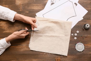 Ahşap kahverengi arka planda kumaş kesen kadın terzinin elleri. Üst görünüm