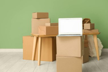 Boş dizüstü bilgisayar, masa ve yeşil duvarın yanındaki kutuları taşıyor.