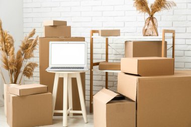 Masada boş dizüstü bilgisayar, taşınan kutular ve beyaz tuğla duvarın yanında otlar var.