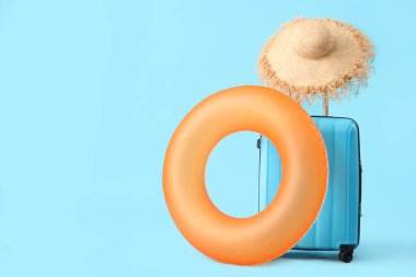 Şişme yüzük, bavul ve mavi arka planda hasır şapka. Seyahat kavramı