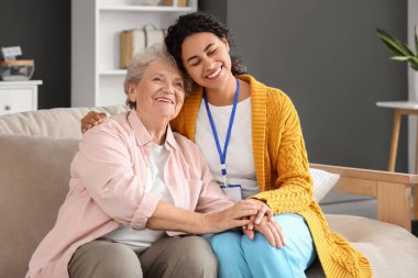 Genç Afro-Amerikalı kadın sağlık görevlisi huzurevinde yaşlı kadına sarılıyor.