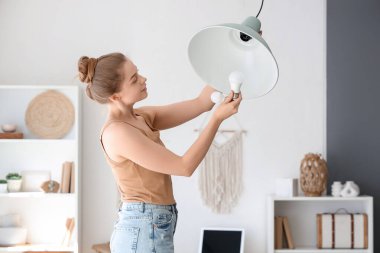 Genç bir kadın evdeki lambaya ampul takıyor.