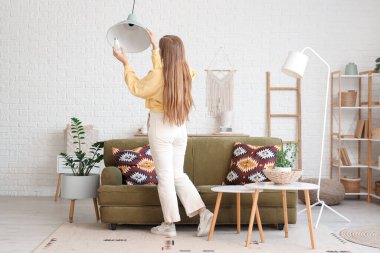 Genç bir kadın evdeki tavan lambasına ampul takıyor.