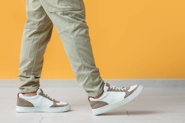 Sarı duvarın yanında şık ayakkabılı genç adam, yakın plan.