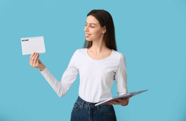 Mavi arka planda takvimi ve defteri olan güzel, mutlu genç bir kadın.