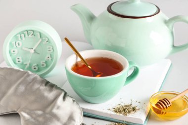 Uyku maskesi, alarm saati ve gri arkaplanda çay seti, yakın plan.