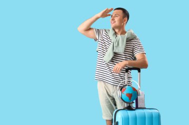 Mavi arka planda bavulu ve küresi olan erkek turist