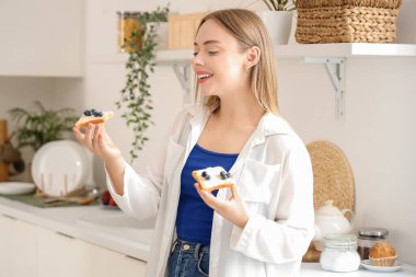 Güzel, genç, mutlu bir kadın mutfakta taze tereyağı ve yaban mersiniyle lezzetli tostlar tutuyor.