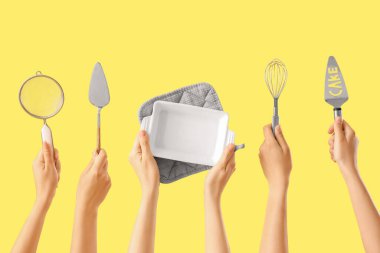 Sarı arka planda farklı pişirme aletleri tutan kadın eller.