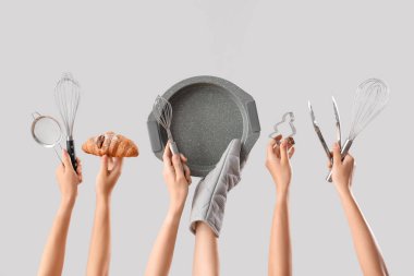 Gri arka planda farklı pişirme aletleri ve lezzetli kruvasanlar tutan kadın eller.