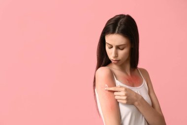 Pembe arka planda krem süren, güneşte yanmış kırmızı tenli güzel bir kadın.