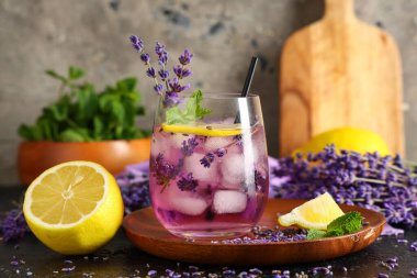 Bir bardak taze lavantalı limonata ve siyah masa üzerinde çiçekler.