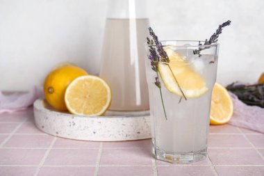 Bir bardak soğuk lavantalı limonata ve renkli fayans masasında limonlar.