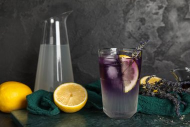 Koyu arkaplanda bir bardak soğuk lavanta, çiçek ve limon.