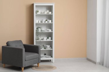 Bulaşıkları ve bej duvarın yanındaki koltuğu olan modern raf ünitesi.