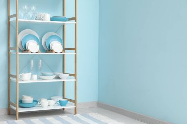 Mutfakta mavi duvarın yanında bulaşık takımı olan modern raf ünitesi.