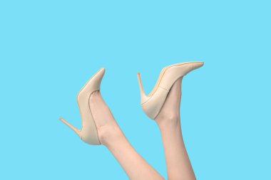 Mavi arka planda, bej renkli yüksek topuklu genç kadın bacakları.